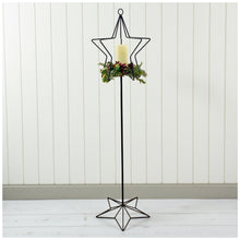 Load image into Gallery viewer, Decorative star-shaped candle holder with a candle with Christmas berries and greenery against a white paneled wall.