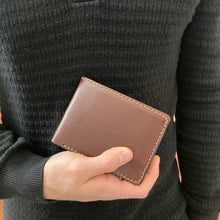 Load image into Gallery viewer, Person holding a brown full grain leather wallet against a dark textured background