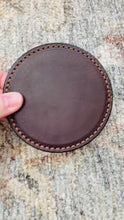 Load and play video in Gallery viewer, Video of a thick brown leather round coaster showing the top and bottom of the coaster and then showing a glass being placed on top of the well made coaster