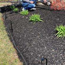 Load image into Gallery viewer, Garden hose running along the edge of a flower bed with garden hooks.  Set of black hose guides are preventing the hose from damaging the plants when the hose is adjusted.