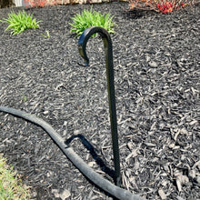 Load image into Gallery viewer, Black plant hose guard placed in the mulch with a black hose running along side of it.
