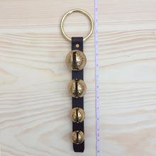 Load image into Gallery viewer, 4 sleigh bells on brass plated ring next to tape measure to show length
