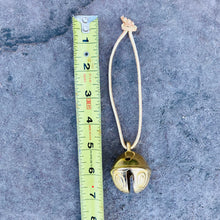 Load image into Gallery viewer, Jingle Bell on leather strap laying next to a measuring tape that measure the bell and leather string length to be approximately 6.75 inches in length
