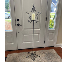 Load image into Gallery viewer, Rustic wrought iron candle holder stand with a white pillar candle candle on a light blue rug in front of a white door.
