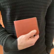 Load image into Gallery viewer, Person holding a brown leather wallet against a dark sweater background
