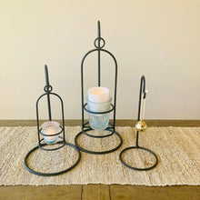 Load image into Gallery viewer, Set of three rustic black metal lantern candle holders on a woven mat with a neutral background
