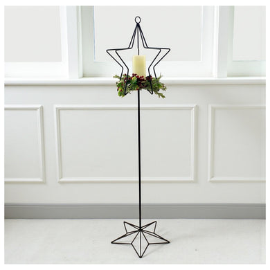 Wrought Iron Tall Candle Stand Christmas Home Decor.  Decorative black metal candle holder with star design against a white paneled wall.