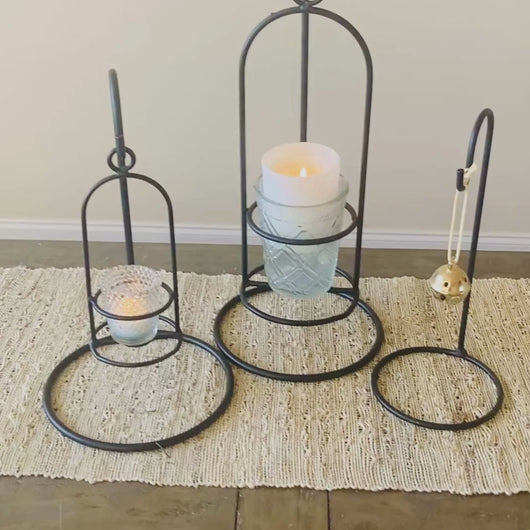 Video that zooms in on each wrought iron hanger hook.  The first medium sized hook holds a small candle jar holder and has a votive candle in it.  The second black metal hook stand holds the large jar candle holder and has a larger candle placed in a glass jar in it.  The last black display stand holds a hanging Christmas bell ornament.  