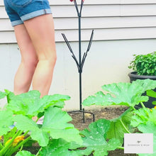Load and play video in Gallery viewer, Video of woman placing the bottle tree stand in her garden by stepping on the base in order to push it into the ground.
