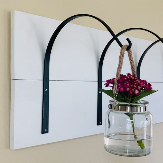 Video of 4 large hooks mounted to white board and holding a small hanging jar with a pink hydrangea.