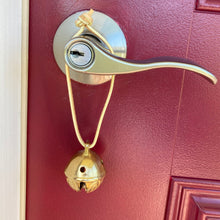 Load image into Gallery viewer, Sleigh bell on leather string hanging from a door knob
