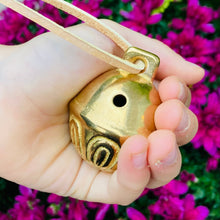 Load image into Gallery viewer, Solid brass bell with leather string in a child&#39;s hand.
