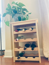 Load image into Gallery viewer, Wine bottle storage rack standing on wooden floor against a light colored wall.  A green plant in a decorative blue pot sits on top of the wine rack.  7 bottles are shown stored in the rack.  Wine bottles not included with wine rack.
